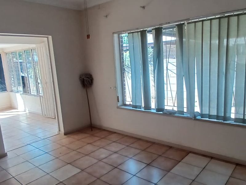 An empty living room featuring tiled flooring, security bars on the windows, and access to an adjacent sunroom or patio area.