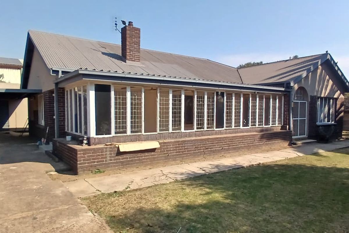 Rear view of a brick house featuring an enclosed sunroom, corrugated metal roof, chimney, and an attached carport with a concrete driveway.