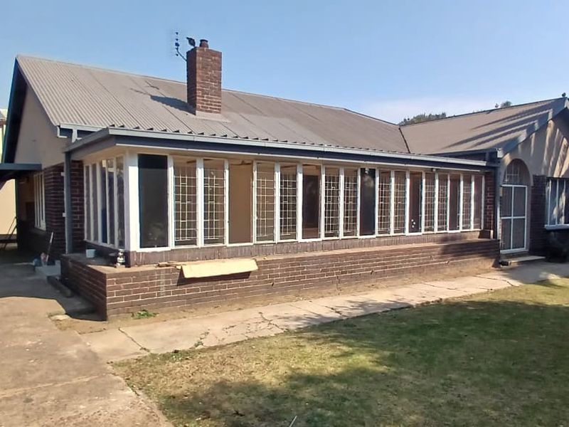 Rear view of a brick house featuring an enclosed sunroom, corrugated metal roof, chimney, and an attached carport with a concrete driveway.