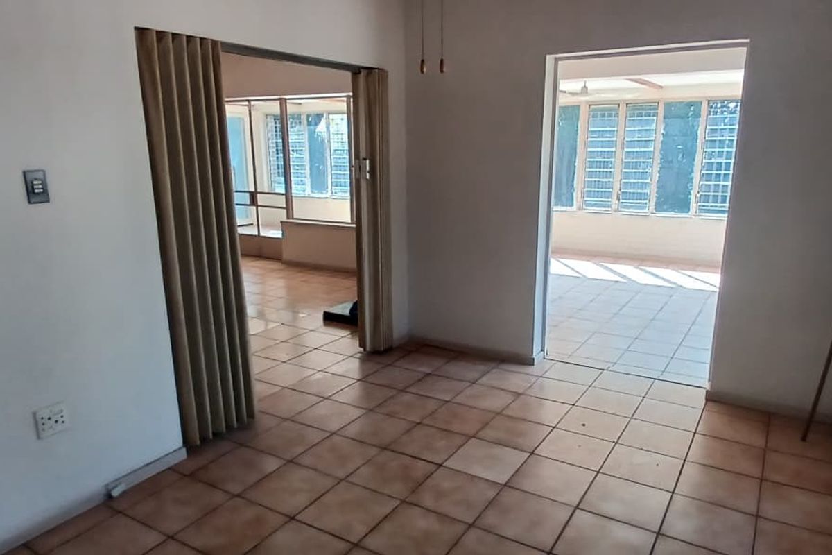 An empty living area featuring ceramic tile flooring, a folding room divider, and access to an adjacent sunroom with louvered windows.