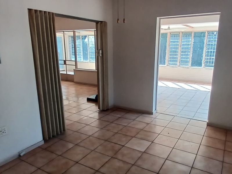 An empty living area featuring ceramic tile flooring, a folding room divider, and access to an adjacent sunroom with louvered windows.