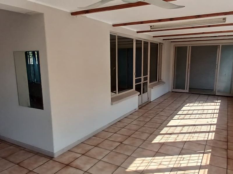 An enclosed patio area featuring tiled flooring, security bars on windows, and a ceiling fan, offering a versatile space for outdoor living.