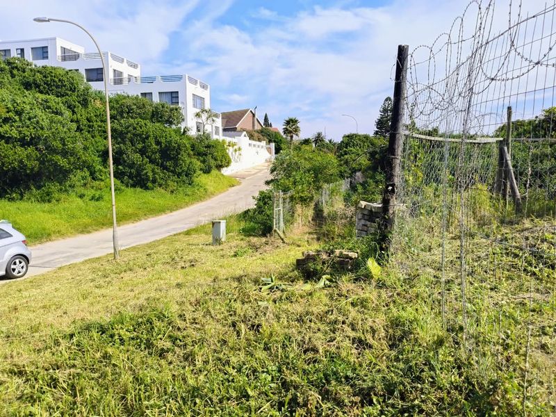 A view of the vacant residential land featuring perimeter wire fencing, adjacent paved street access, and surrounding established neighborhood vegetation.