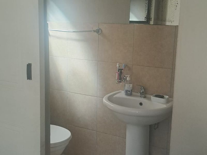 A functional bathroom featuring a pedestal basin, toilet, and neutral wall tiling. The space is compact and includes a wall-mounted mirror.