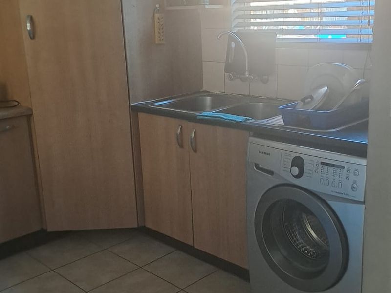 A functional laundry area featuring tiled flooring, built-in cabinetry, a double sink, and a window with venetian blinds.
