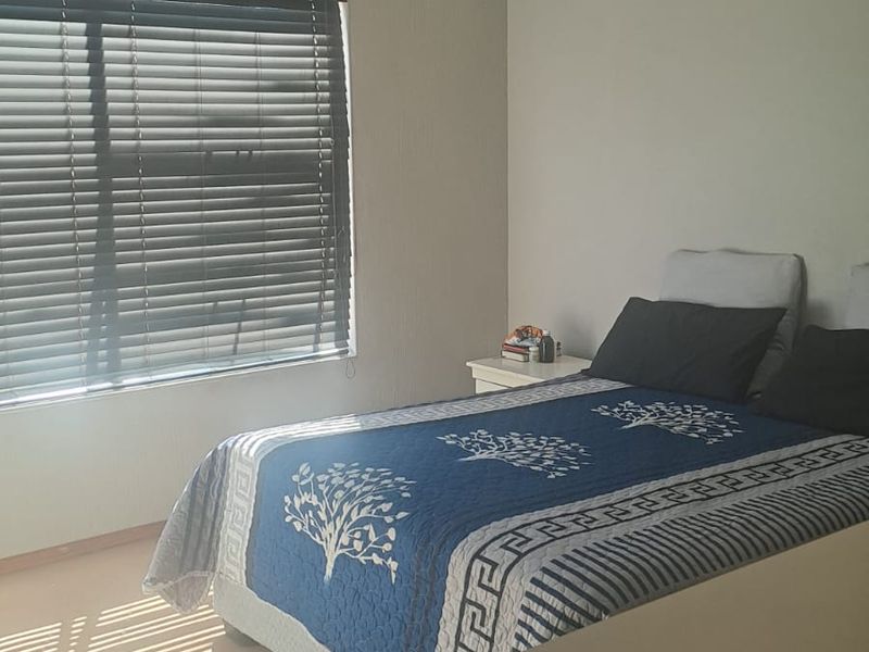 A functional bedroom featuring neutral wall finishes, a window with venetian blinds, and a ceiling-mounted spotlight fixture.