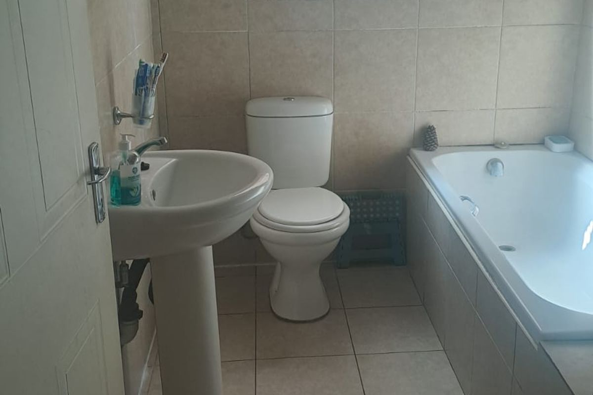 A functional bathroom featuring a pedestal basin, toilet, and built-in bathtub with neutral wall and floor tiling.