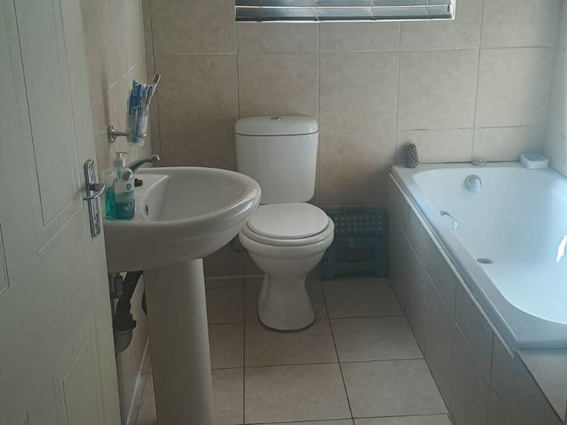 A functional bathroom featuring a pedestal basin, toilet, and built-in bathtub with neutral wall and floor tiling.