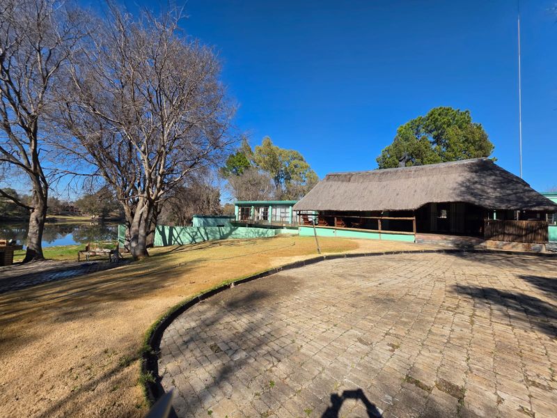 Rear view of the property featuring a thatched roof structure, paved driveway, and a lawn area overlooking the water.