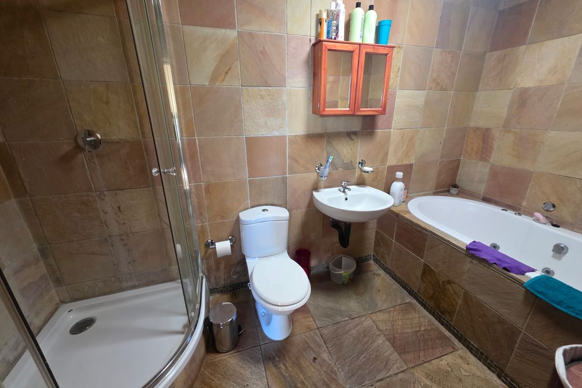 A functional bathroom featuring a corner shower, built-in bathtub, wall-mounted basin, and toilet, finished with natural stone wall and floor tiling.