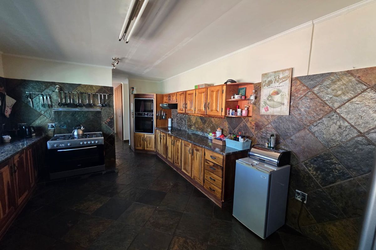 A spacious kitchen featuring extensive wooden cabinetry, stone tile flooring, and a stone backsplash, equipped with a built-in oven and gas stove.