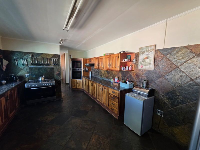 A spacious kitchen featuring extensive wooden cabinetry, stone tile flooring, and a stone backsplash, equipped with a built-in oven and gas stove.