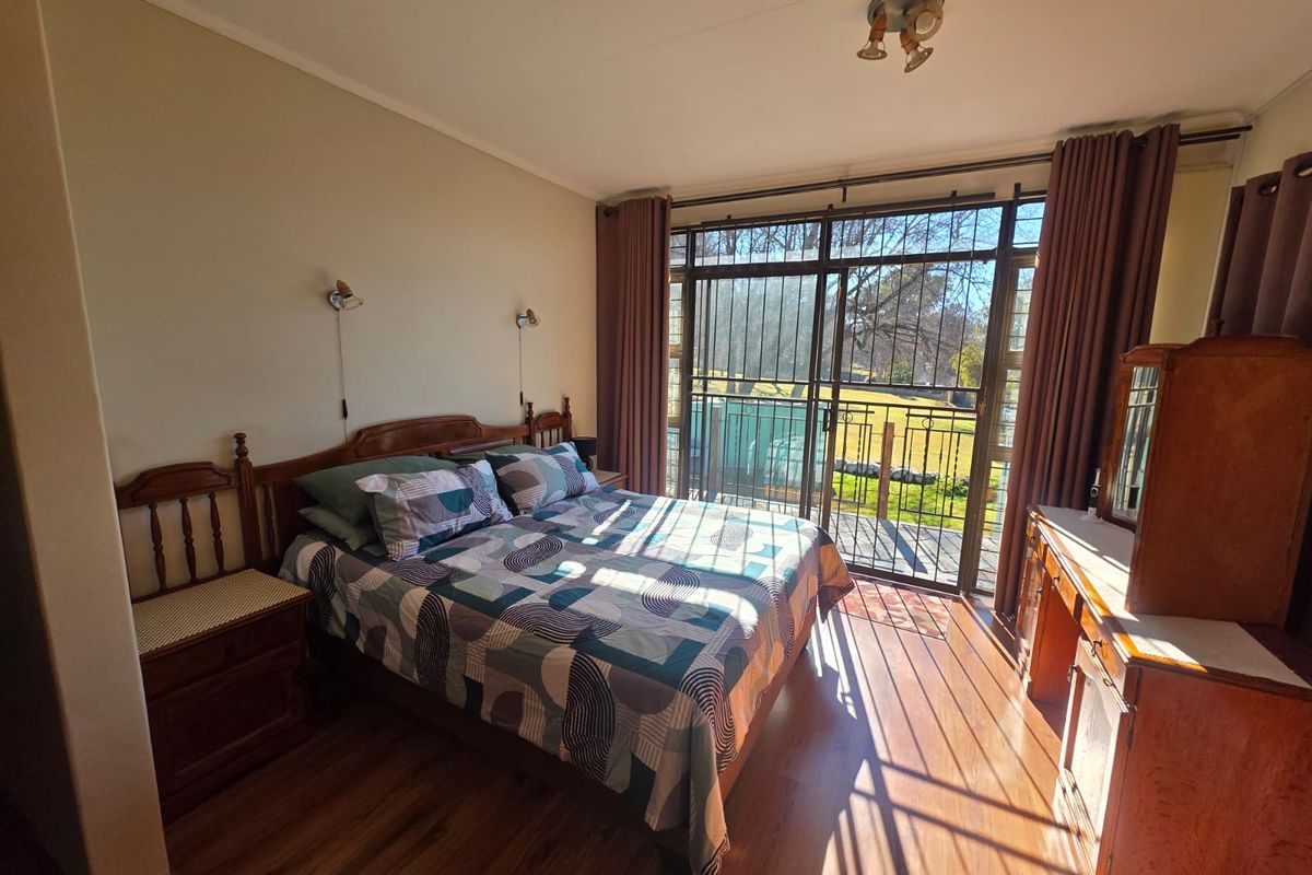 A bedroom featuring laminate flooring, wall-mounted lighting, and a large sliding glass door with security gate providing access to the outdoors.