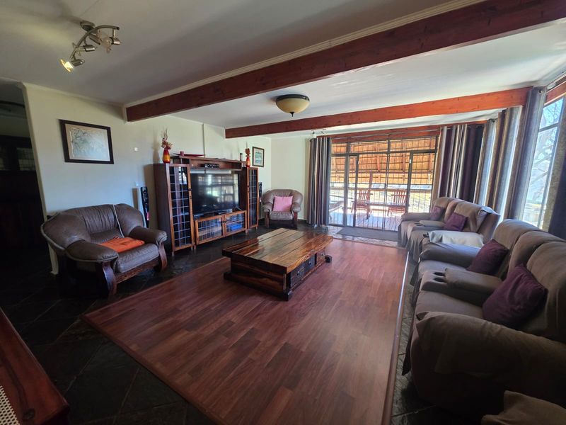 Spacious living room featuring exposed timber ceiling beams, a mix of slate and laminate flooring, and direct access to an outdoor patio area.