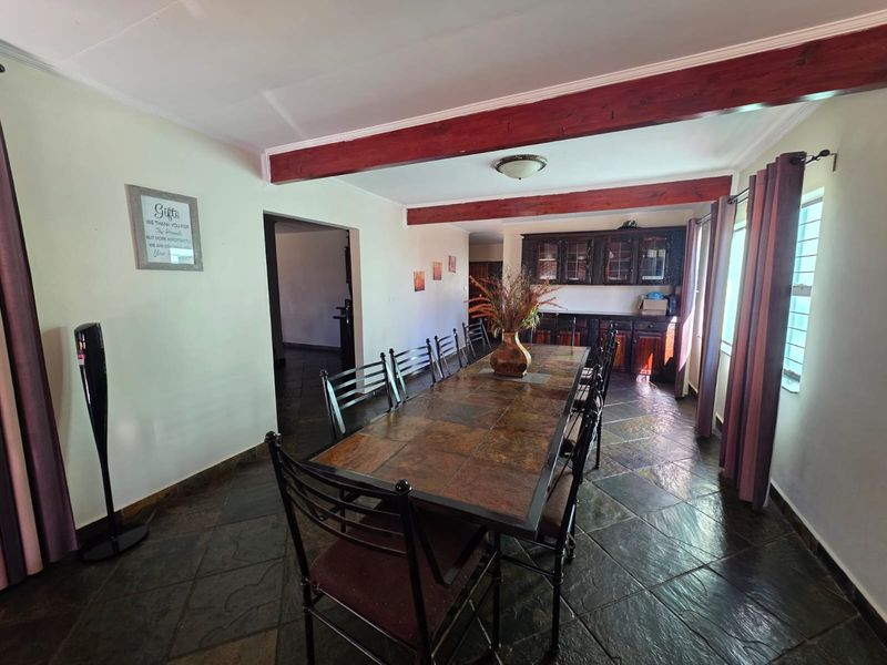 Spacious dining room featuring rustic slate tile flooring, exposed timber ceiling beams, and integrated wooden cabinetry for storage.