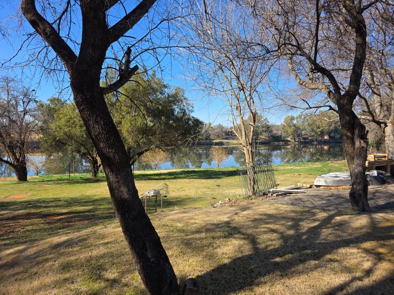 A scenic view of the riverfront property featuring mature trees and expansive lawn area, offering a peaceful outdoor setting.