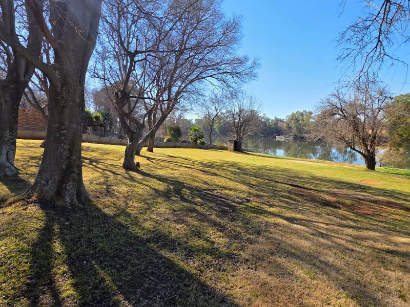 A scenic view of a spacious, tree-lined lawn leading down to a tranquil waterfront area.