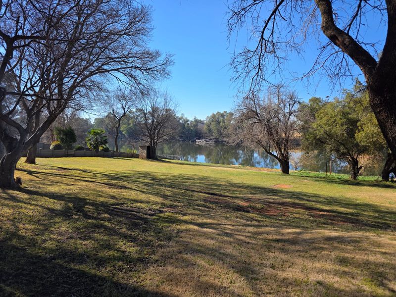 A scenic view of a tranquil riverfront property featuring expansive lawns and mature trees, offering a peaceful outdoor setting.