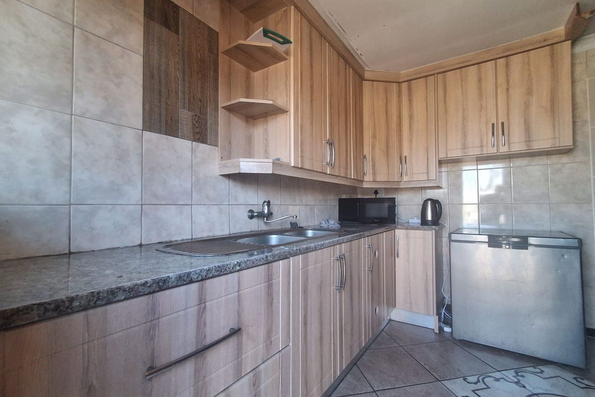 A functional kitchen featuring light wood-look cabinetry, granite-style countertops, stainless steel sink, and neutral ceramic wall and floor tiling.