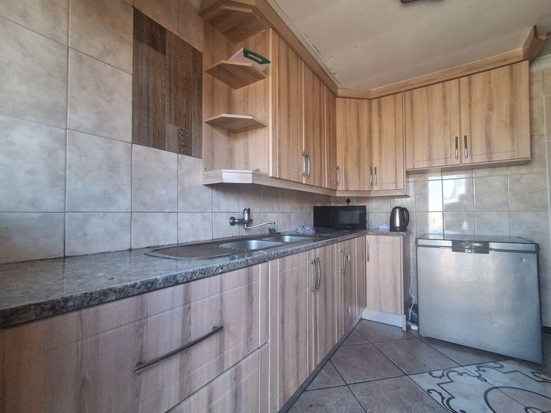 A functional kitchen featuring light wood-look cabinetry, granite-style countertops, stainless steel sink, and neutral ceramic wall and floor tiling.