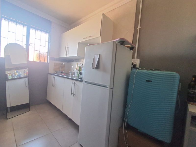 A compact kitchen featuring white built-in cabinetry, a stainless steel sink, and tiled flooring, requiring some finishing work on walls and electrical fixtures.