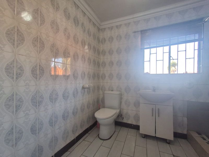 A functional bathroom featuring tiled walls, a vanity basin, and a toilet, with natural light provided by a window with security bars.