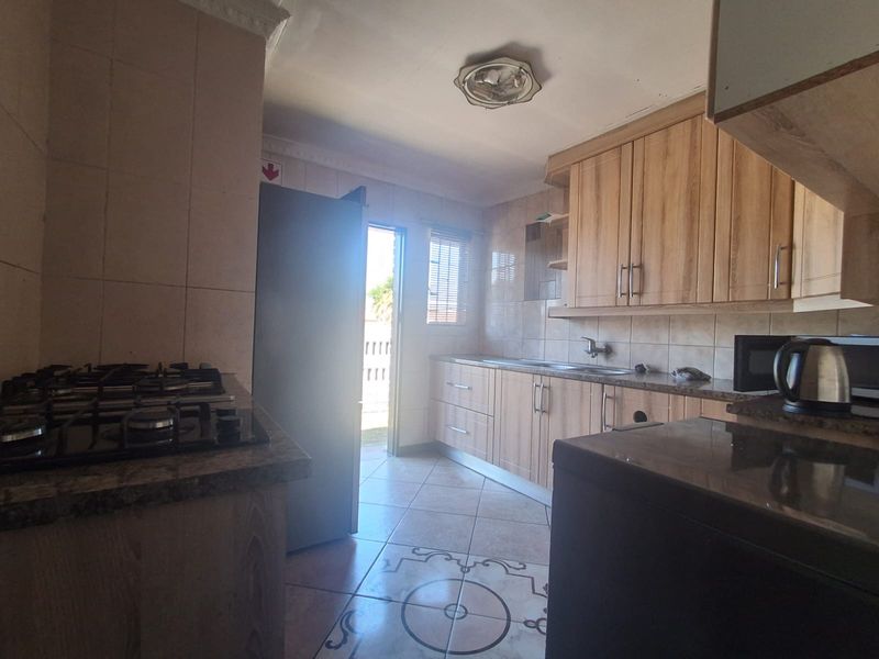 A functional kitchen featuring wood-look cabinetry, granite countertops, a gas hob, and tiled flooring with direct access to the exterior.