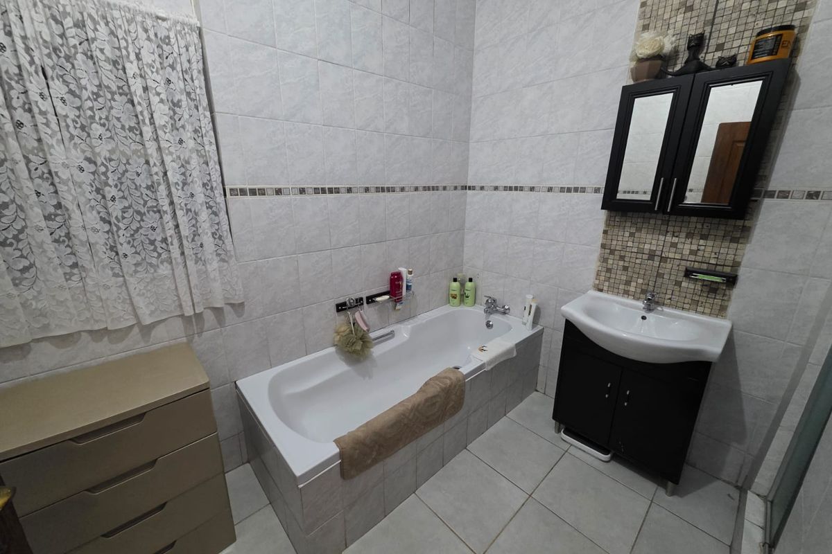 A functional bathroom featuring a built-in bathtub, a vanity cabinet with a basin, and tiled walls and flooring.