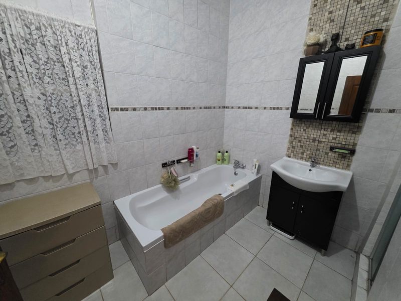 A functional bathroom featuring a built-in bathtub, a vanity cabinet with a basin, and tiled walls and flooring.