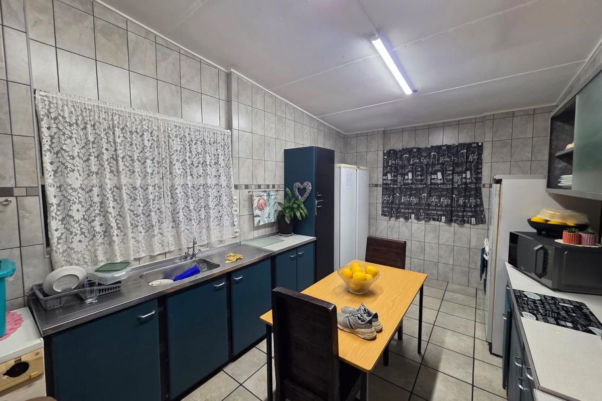 A functional kitchen featuring tiled walls and flooring, built-in cabinetry, and a stainless steel sink, offering a practical layout for daily use.