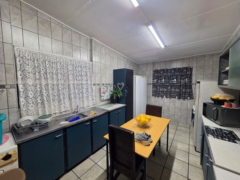 A functional kitchen featuring tiled walls and flooring, built-in cabinetry, and a stainless steel sink, offering a practical layout for daily use.
