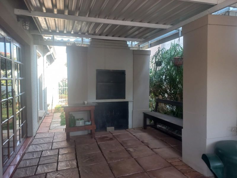 Covered patio area featuring a built-in braai, paved flooring, and direct access to the interior through sliding glass doors.