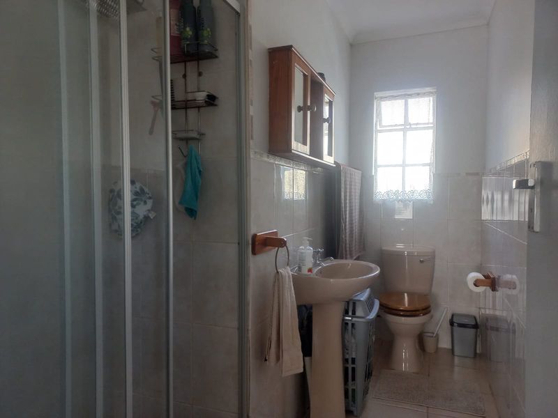 A functional bathroom featuring a shower enclosure, pedestal basin, toilet, and wall-mounted storage cabinet with tiled wall finishes.