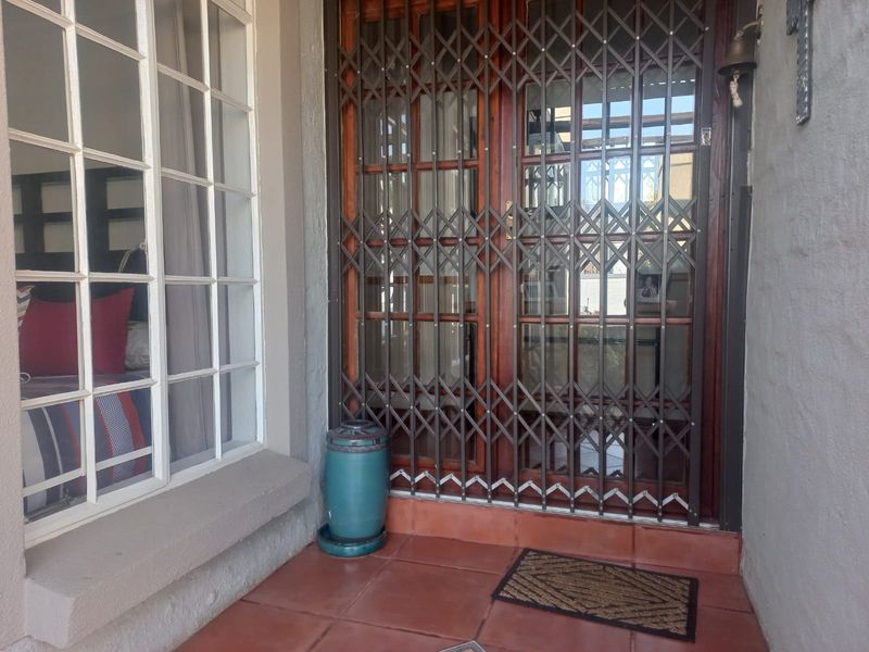 A covered patio area featuring terracotta floor tiles, a secure metal gate, and a wooden framed glass door leading into the home.