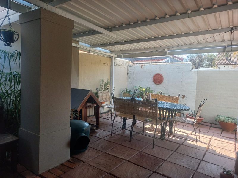 A covered outdoor patio area featuring paved flooring, a structural masonry pillar, and a corrugated metal roof, enclosed by a perimeter boundary wall.