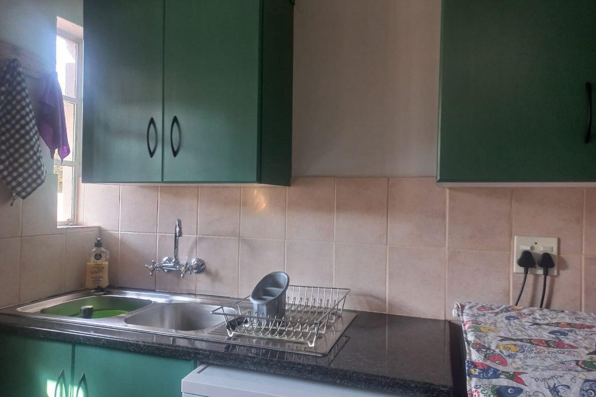 A functional kitchen area featuring green cabinetry, a double sink with wall-mounted tap, and tiled backsplash with dark laminate countertops.