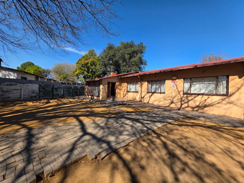 Rear view of the property featuring a paved walkway, established trees, and a secure perimeter wall.