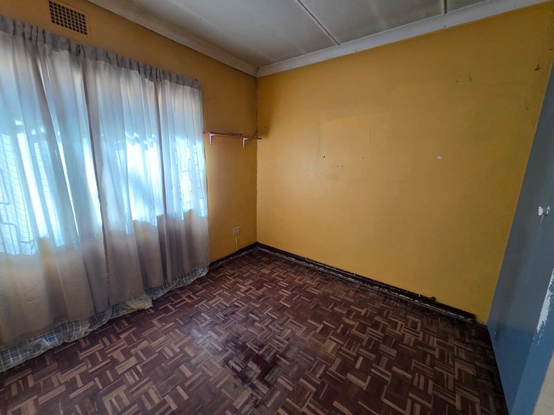 An empty bedroom featuring original parquet flooring, yellow painted walls, and a ceiling ventilation vent, requiring cosmetic updates and refurbishment.