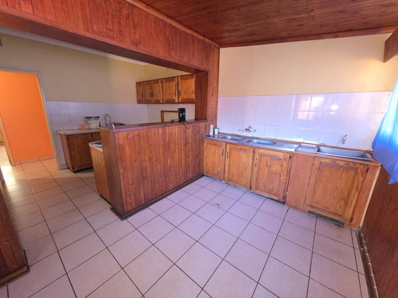 A dated kitchen featuring wooden cabinetry, tiled flooring, and a tiled backsplash, offering a functional layout ready for modernization.
