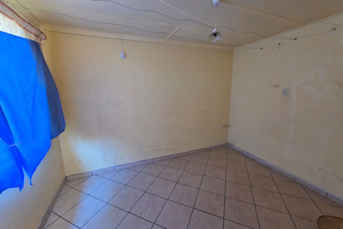 An empty bedroom featuring tiled flooring and basic lighting, currently requiring cosmetic updates and wall repairs.