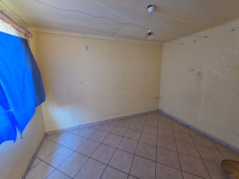 An empty bedroom featuring tiled flooring and basic lighting, currently requiring cosmetic updates and wall repairs.