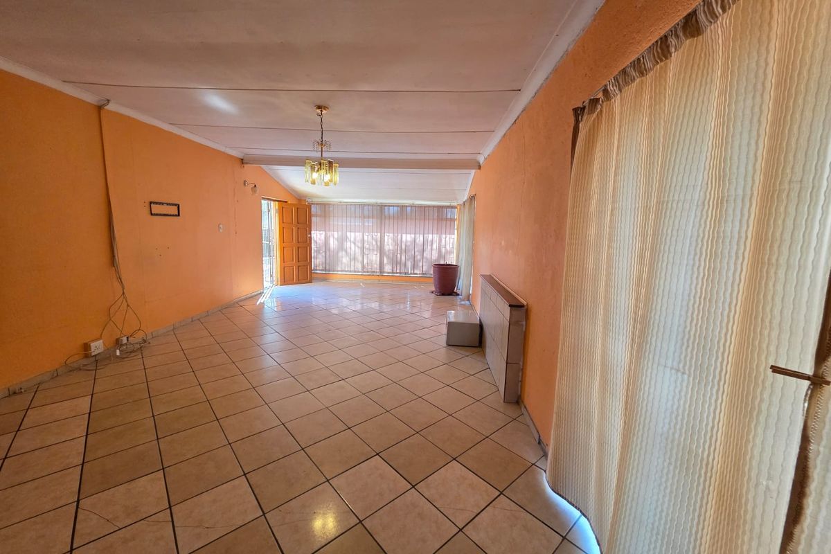 An empty living room featuring ceramic floor tiles, a ceiling light fixture, and access to an outdoor area through a sliding glass door.