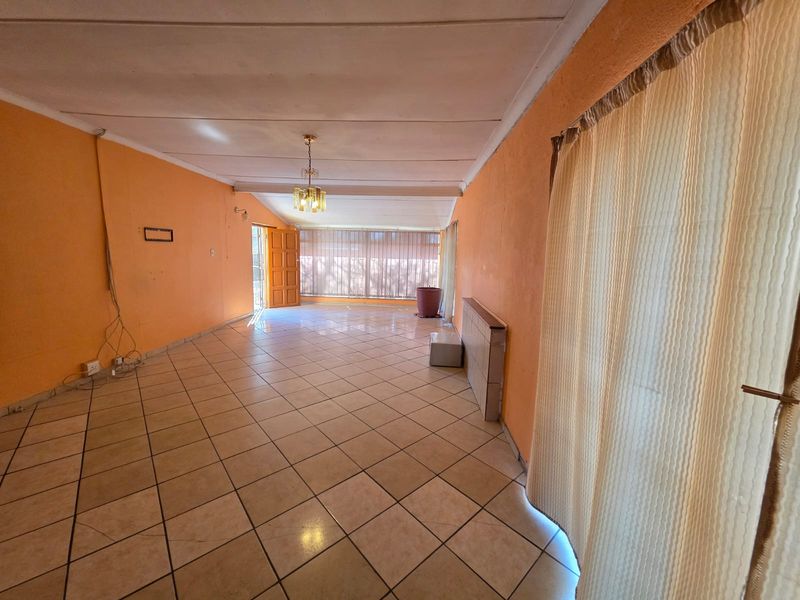 An empty living room featuring ceramic floor tiles, a ceiling light fixture, and access to an outdoor area through a sliding glass door.