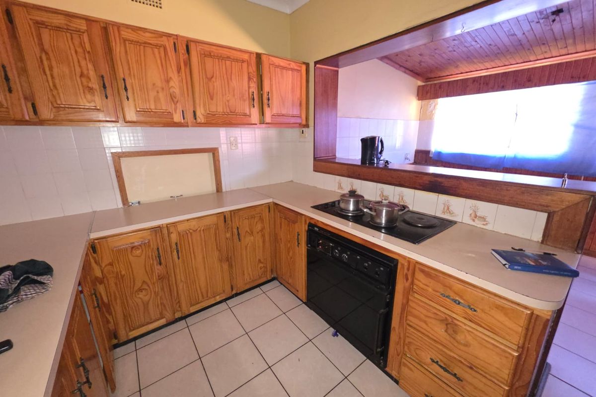 A functional kitchen featuring timber cabinetry, laminate countertops, and a built-in electric hob and oven, with a pass-through window to the adjacent living area.