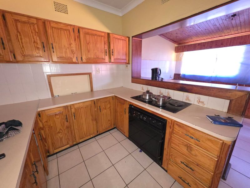 A functional kitchen featuring timber cabinetry, laminate countertops, and a built-in electric hob and oven, with a pass-through window to the adjacent living area.