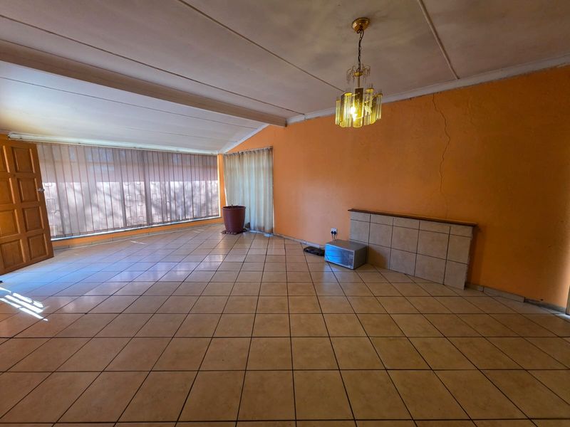 Spacious living area featuring tiled flooring, a tiled feature wall, and a ceiling light fixture, presenting a blank canvas for renovation.