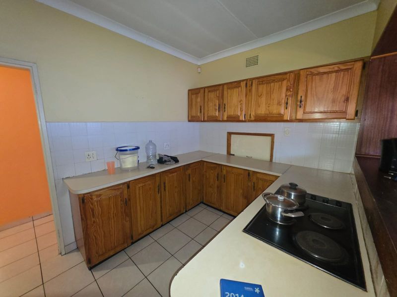 A functional kitchen featuring traditional wooden cabinetry, laminate countertops, an integrated electric hob, and tiled flooring with a neutral backsplash.