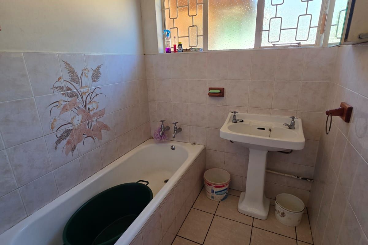 A dated bathroom featuring a pedestal basin, built-in bathtub, and tiled finishes, requiring cosmetic updates to improve its overall condition and appeal.