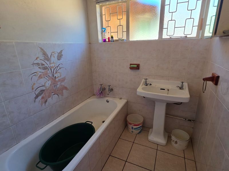 A dated bathroom featuring a pedestal basin, built-in bathtub, and tiled finishes, requiring cosmetic updates to improve its overall condition and appeal.