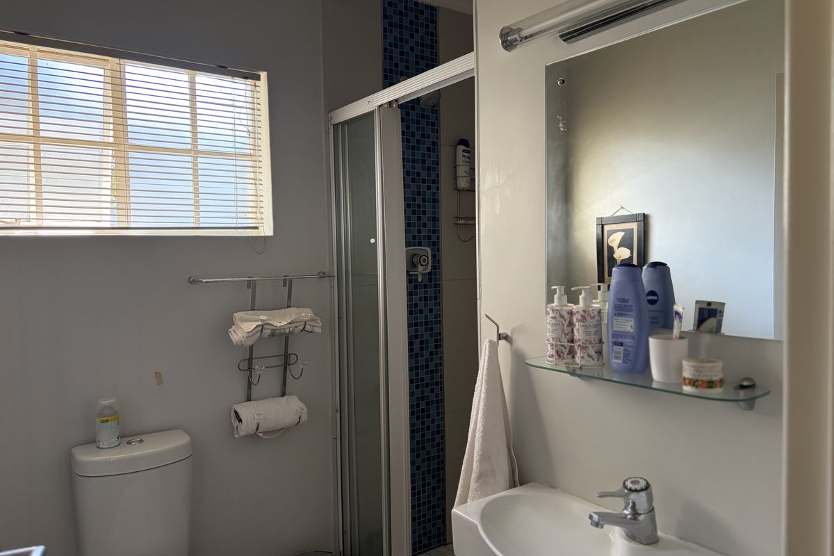 A functional bathroom featuring a shower enclosure with mosaic tiling, a vanity basin with a mirror, and a standard toilet.